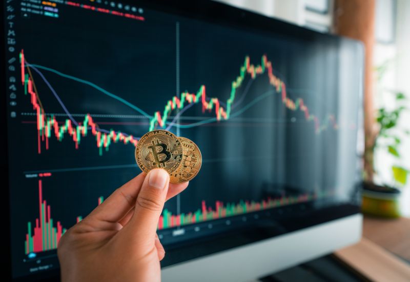 Bitcoins in hand and crypto trading graphic behind